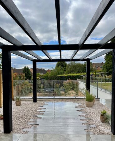 A dark pergola framing a paved garden walkway with gravel borders.