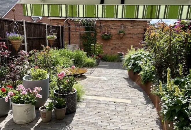 A courtyard garden with curved raised beds, layered planting and grey paving.