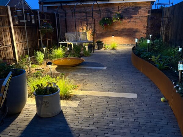 Curved planted beds and a paved courtyard lit with warm garden lighting.